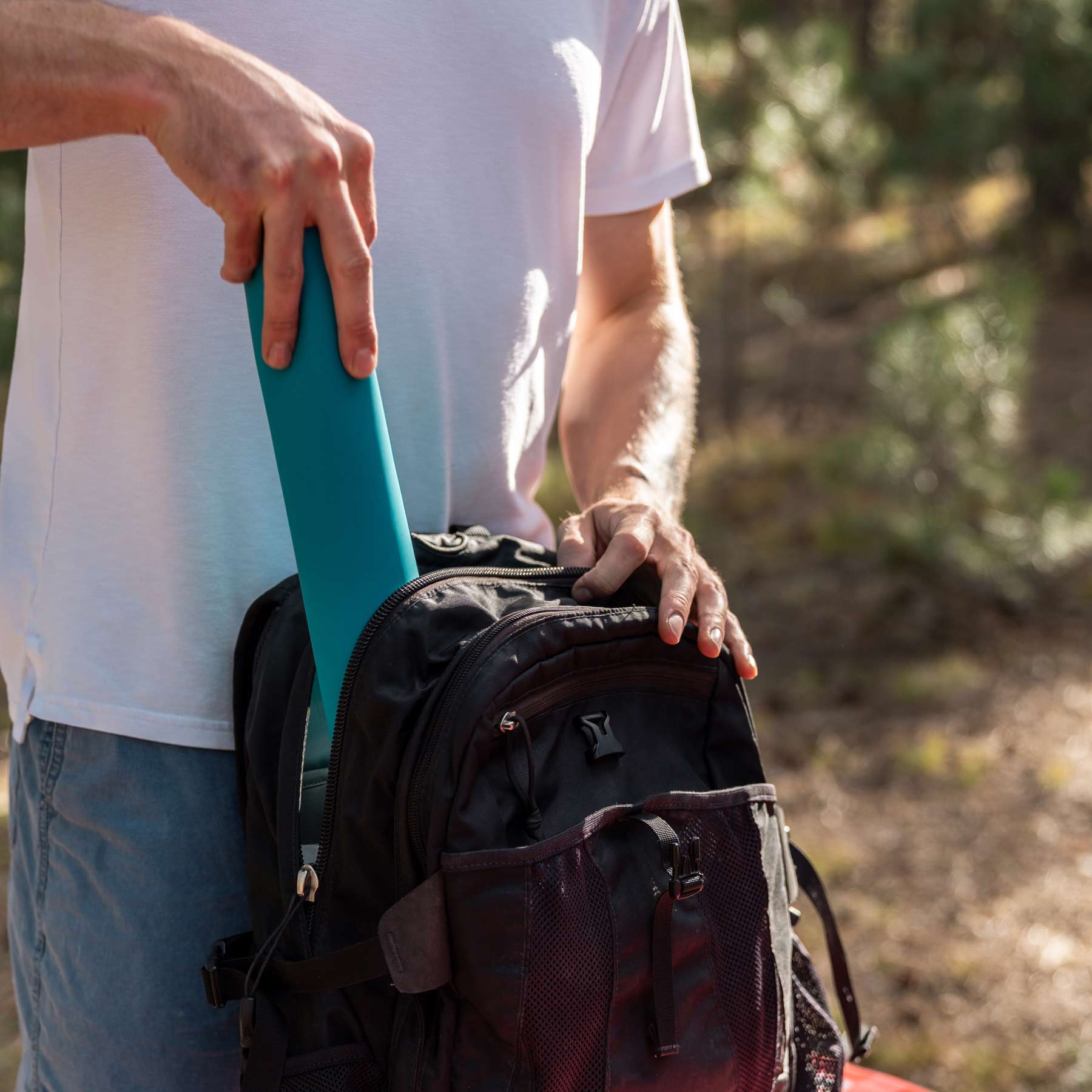 Image shows a person putting the Adventure Ready Compact Dish Drying Station into his pack, rolled up.