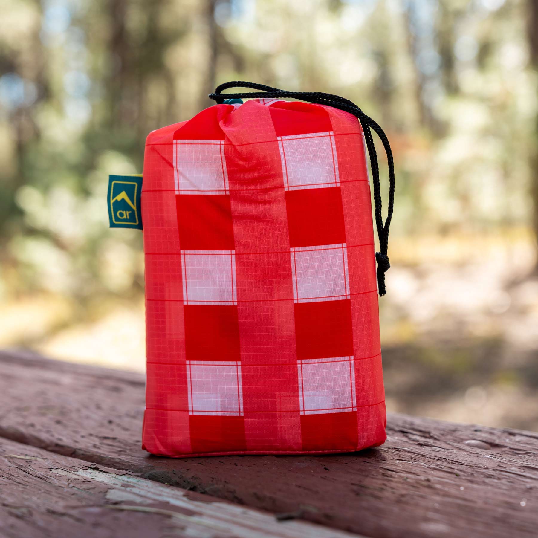 Image shows the AR Picnic Tablecloth in a stuff sack on top of a picnic table.