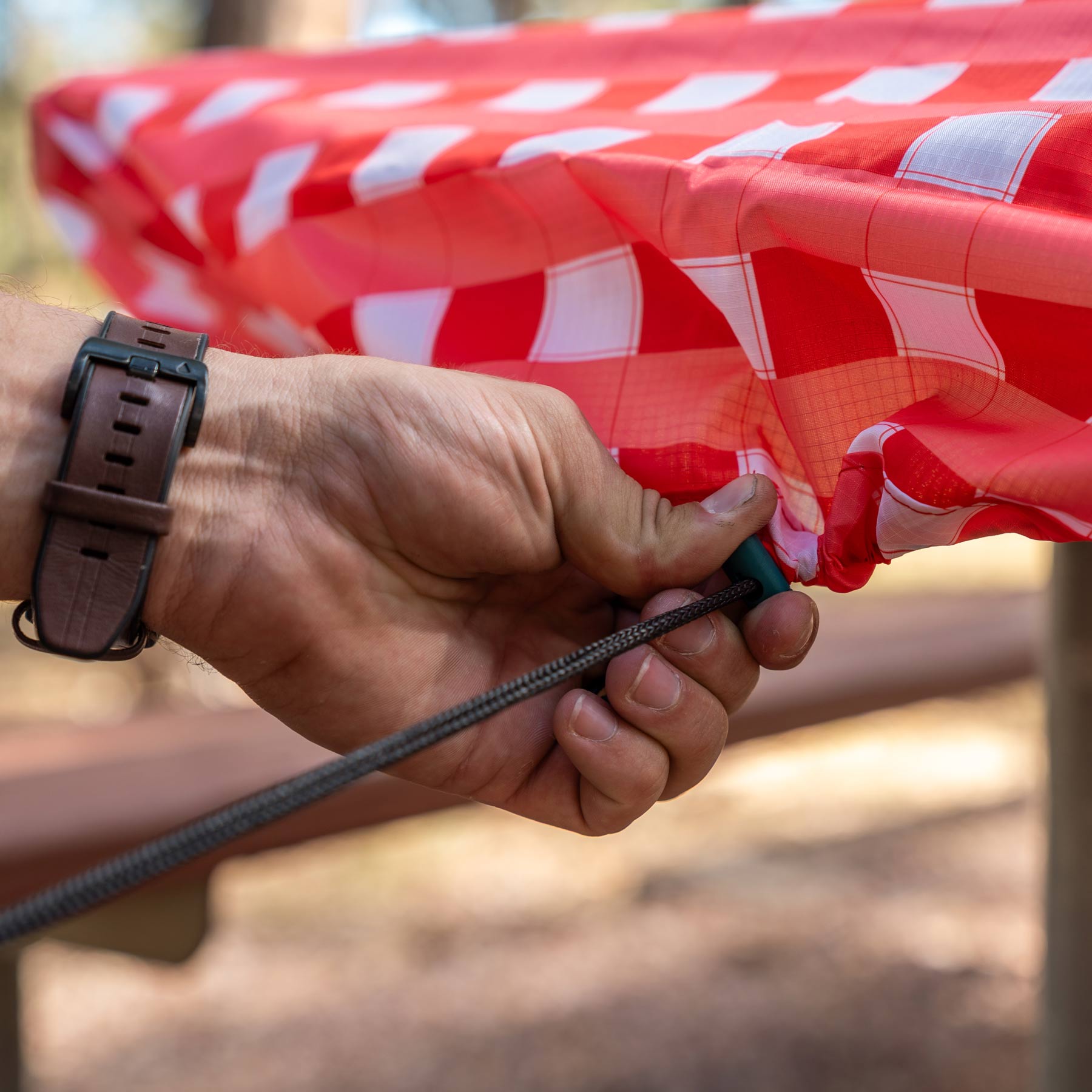 The image shows a person adjusting the picnic tablecloth onto the table with the built-in drawcord.