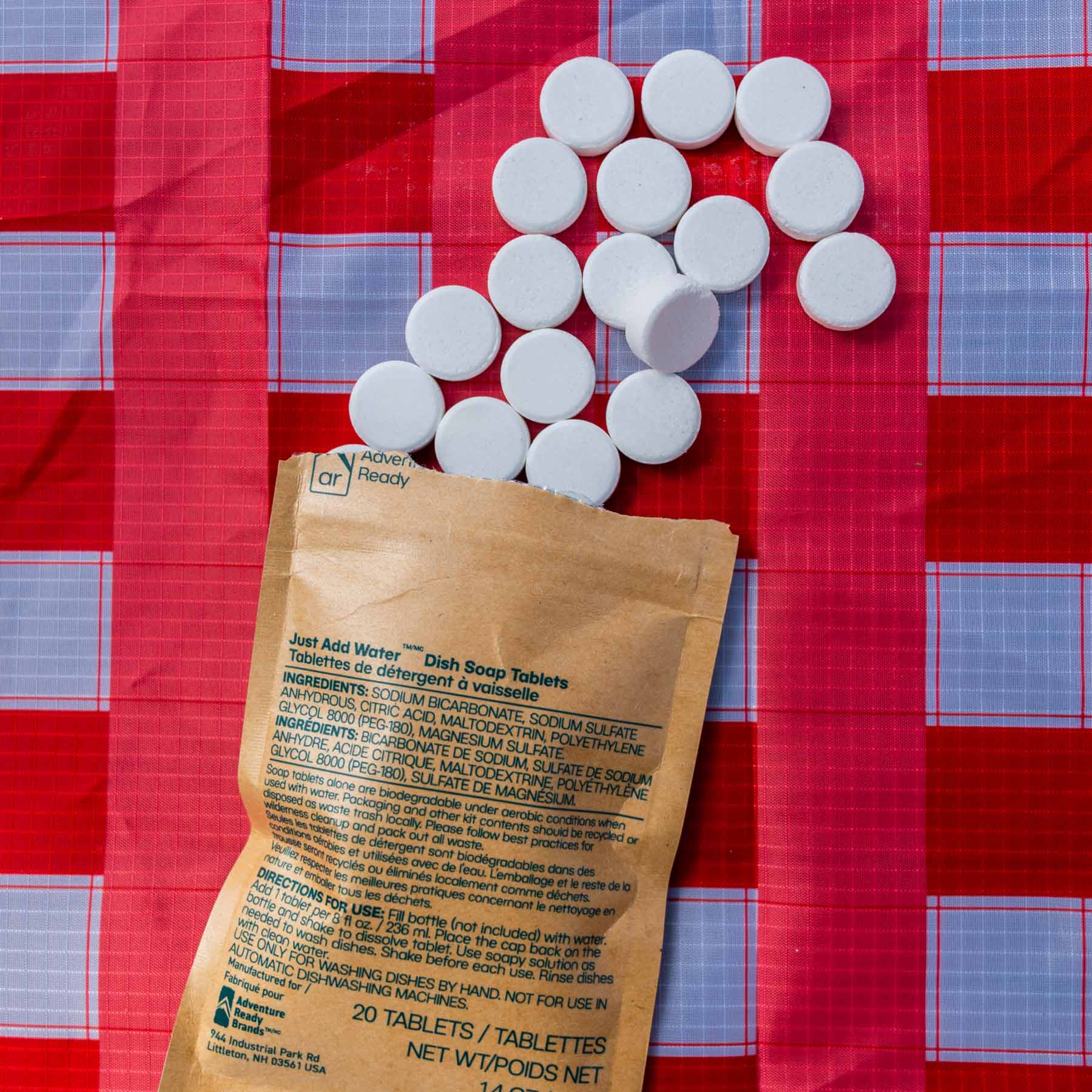 A pack of the Just Add Water Dish Soal Tablets opened and tablets poured out on top of the Adventure Ready Picnic Table Cloth.