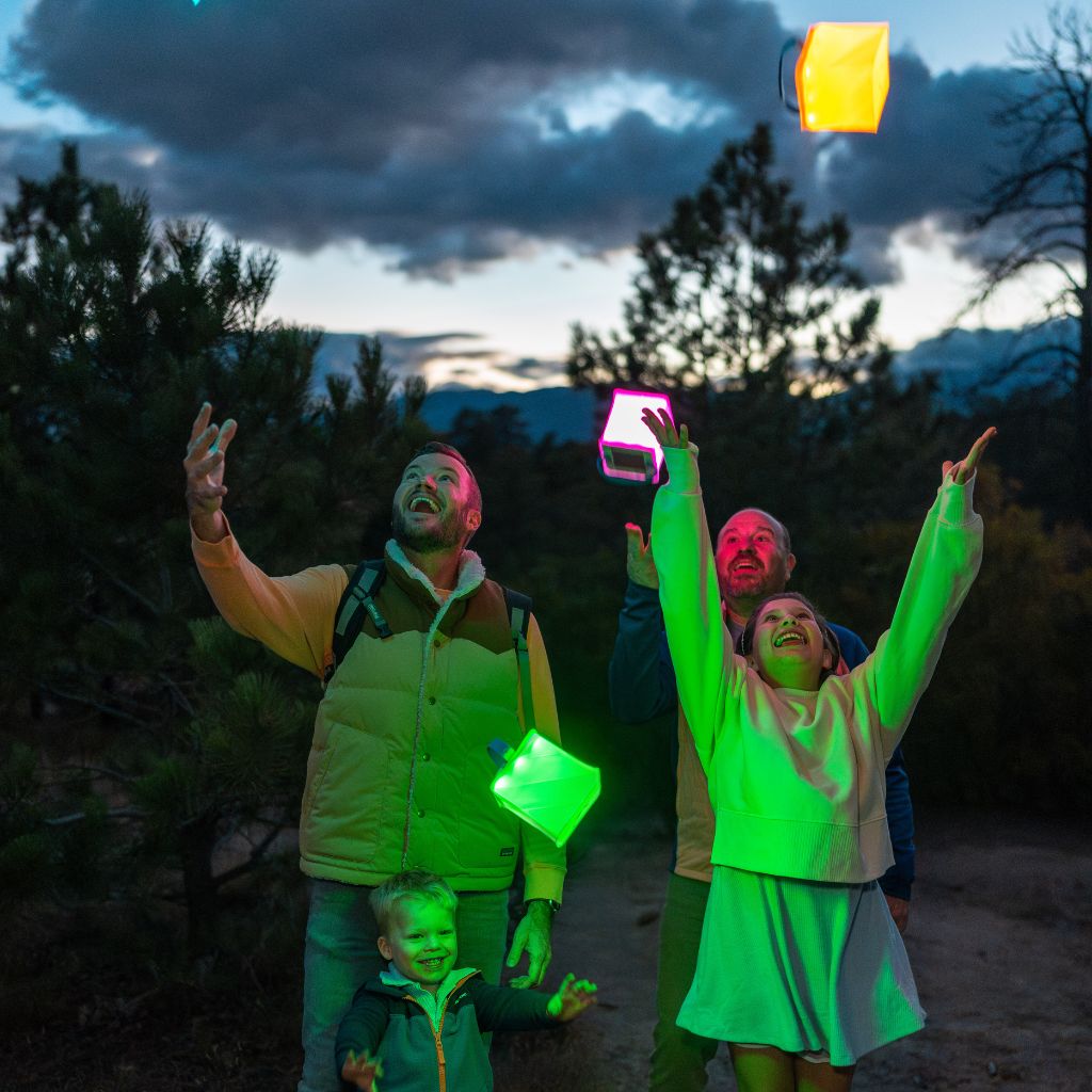 A smiling family throwing colorful lanterns in the air at a campsite