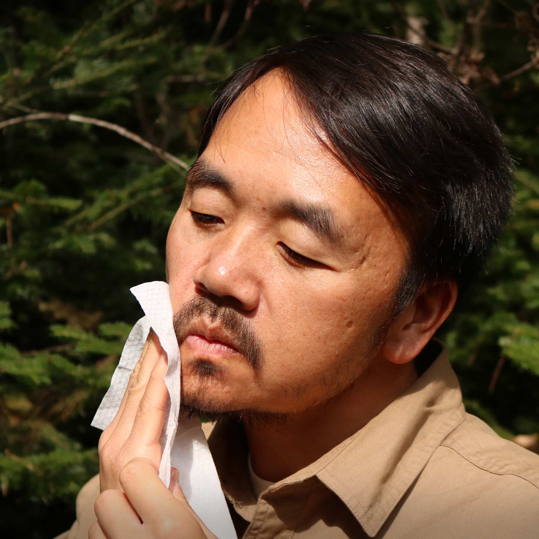 A man wiping his face in the woods with the Adventure Ready Wildly Clean Wipe.